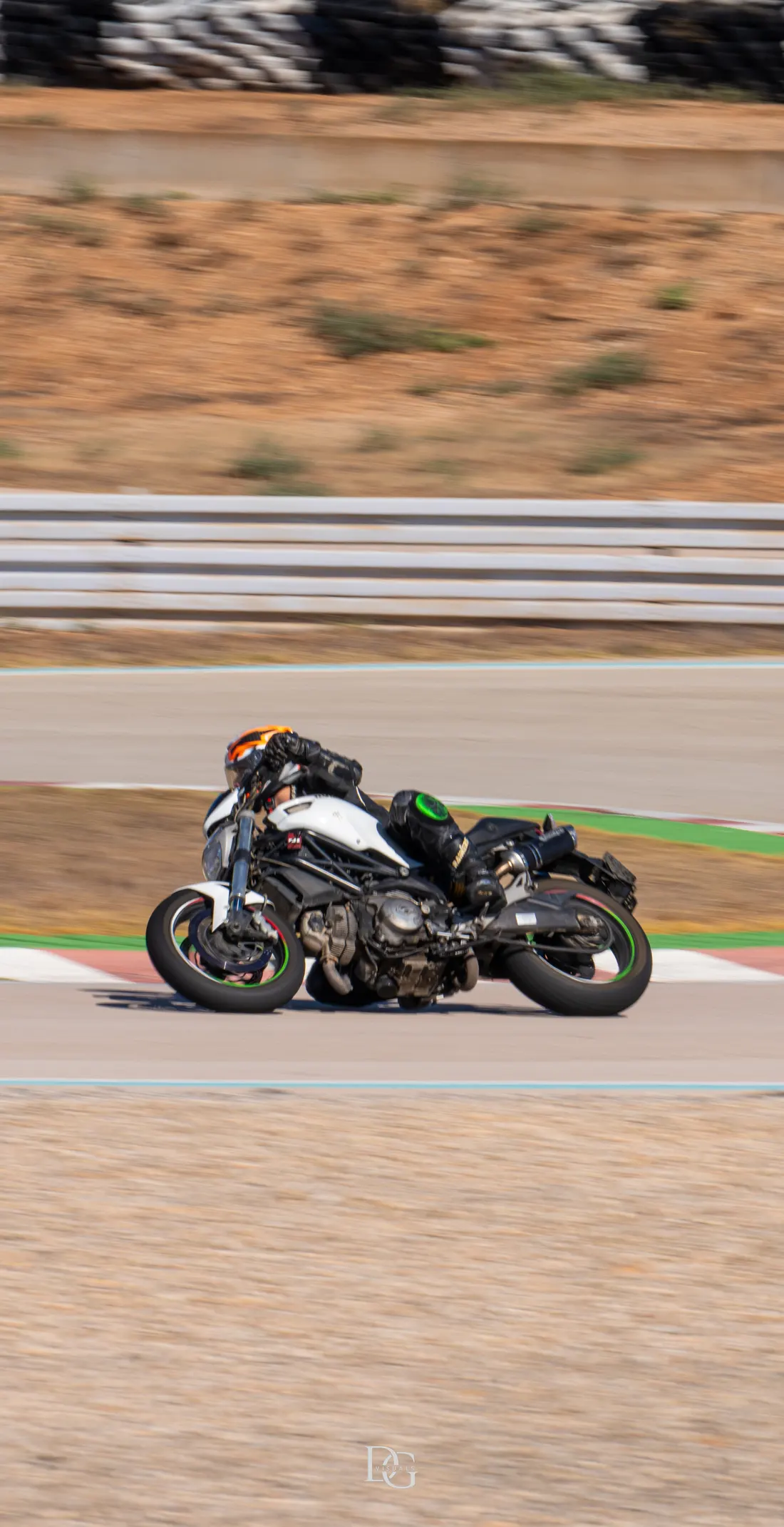 Moto blanca tumbada en curva con piloto de casco naranja